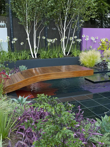 A modern contemporary garden design with flower borders, decking a water feature