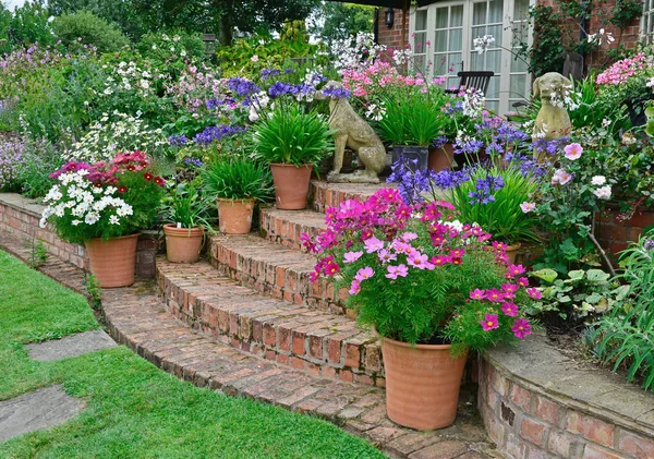 Colourful garden terrace with mixed flower beds and planted containers making a very attractice display in front of a country house
