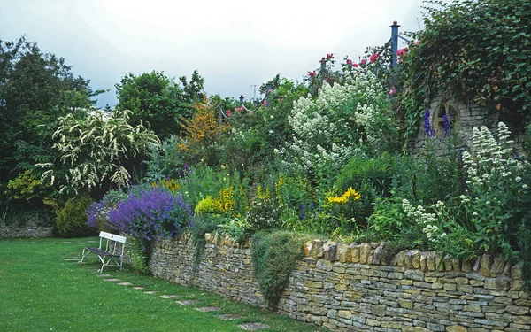 Banc de jardin sur pelouse devant un lit surélevé dans un jardin de campagne — Photo