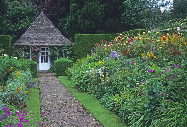 Camino que conduce a la sala de jardín bordeada de coloridas fronteras en un jardín rural —  Fotos de Stock