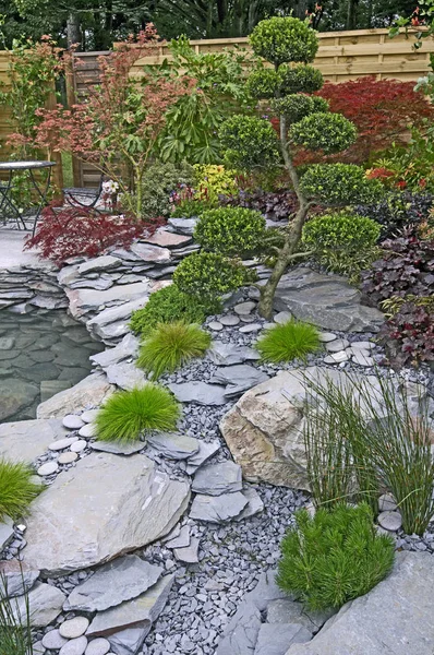 Tuin met water, rots, Topiarium en gemengde aanplant — Stockfoto