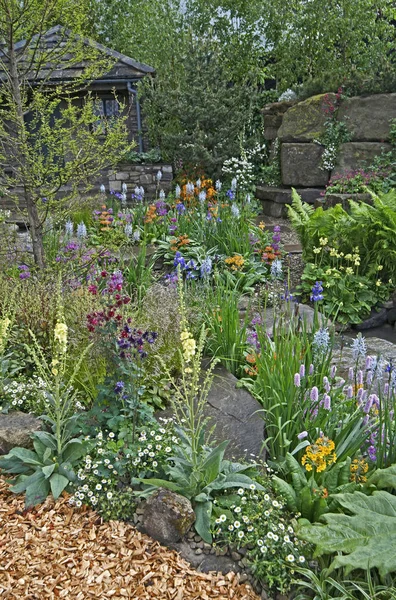 Une maison de campagne et un jardin situés dans une rocaille boisée avec une exposition colorée de fleurs — Photo