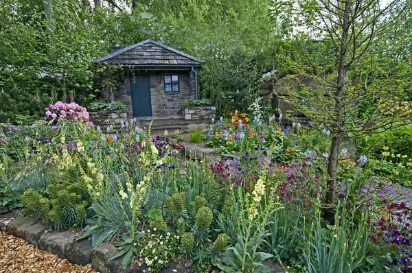Una casa de campo y jardín situado en una rocalla arbolada con una colorida muestra de flores — Foto de Stock