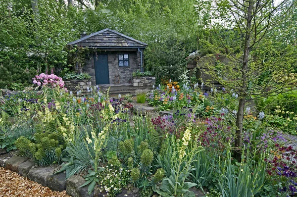 Une maison de campagne et un jardin situés dans une rocaille boisée avec une exposition colorée de fleurs — Photo