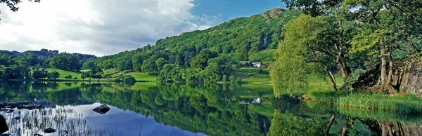 L agua tranquila y tranquila de Loughrigg Tarn con árboles reflectantes cerca de Windermere en el Distrito de los Lagos Cumbria Inglaterra — Foto de Stock