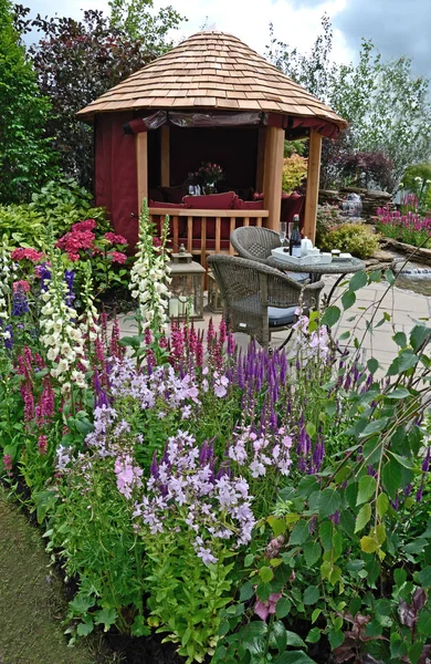 La zona del patio con asientos en un jardín acuático con borde de flores de colores —  Fotos de Stock