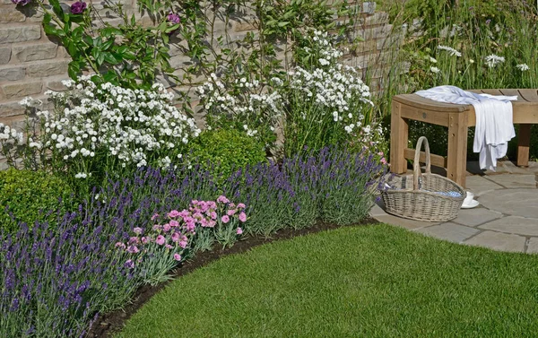 Primo piano di un bordo di fiore in un angolo di un giardino di cottage murato con cesto e pausa caffè — Foto Stock