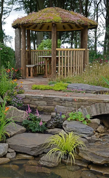 Een aantrekkelijke watertuin met zandsteen rotsbrug en een houten zomerhuis met een Sedum dak — Stockfoto