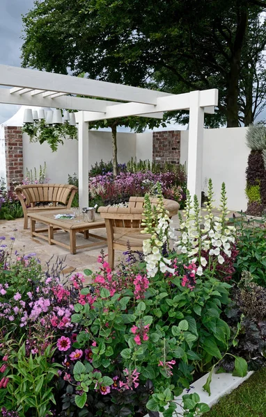 A contemporary garden with terraced area and stylish wooden furniture surrounded by colourful flowering borders