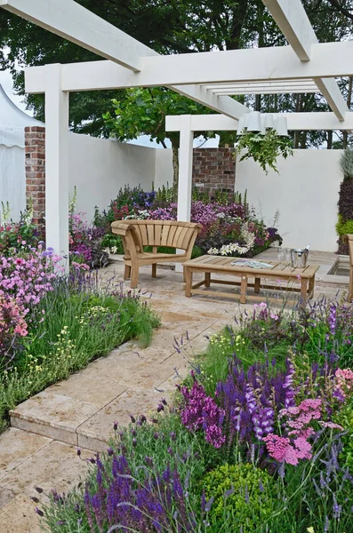 Ein zeitgenössischer Garten mit Terrassenfläche und stilvollen Holzmöbeln umgeben von farbenfrohen blühenden Rändern — Stockfoto