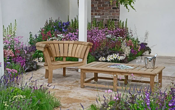 Ein zeitgenössischer Garten mit Terrassenfläche und stilvollen Holzmöbeln umgeben von farbenfrohen blühenden Rändern — Stockfoto