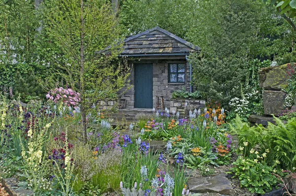 A country cottage and garden situated in a wooded rockery with a colourful display of flowers — Stock Image A country cottage and garden situated in a wooded rockery with a colourful display of flowers Stock Image