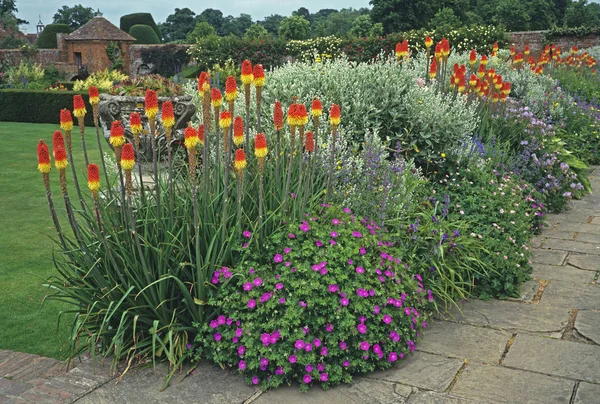 Un impressionante e colorato bordo floreale terrazzato con Kniphofia caulescens in un giardino inglese casa di campagna — Foto Stock