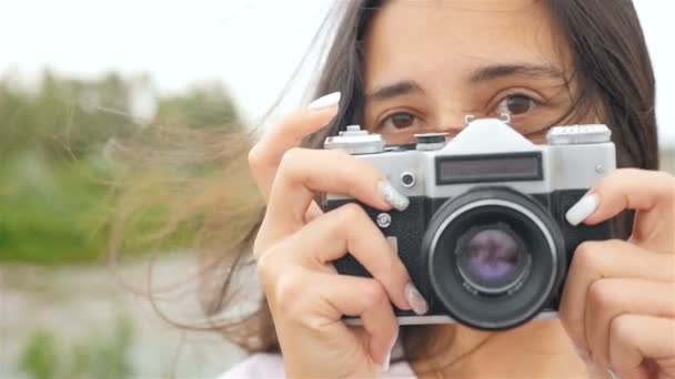 Uma linda garota segura uma câmera e tira fotos. Close-up — Vídeo de Stock