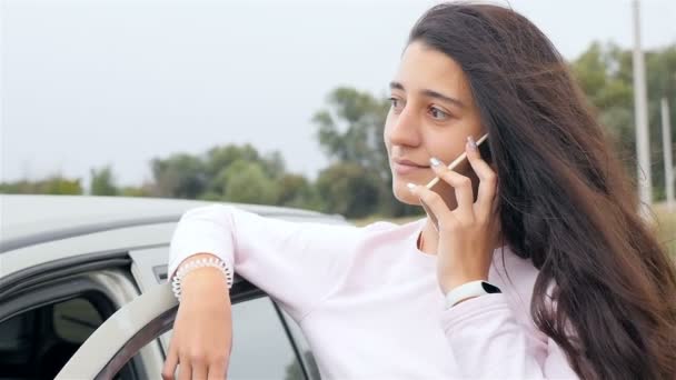 Молода і красива дівчина розмовляє по телефону біля машини. Гарна посмішка на обличчі. Крупним планом. Повільний рух — стокове відео
