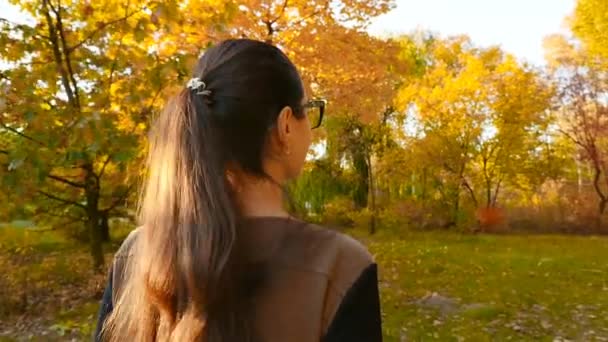 Una bella bruna con gli occhiali cammina attraverso la foresta autunnale. Bellissimi alberi. Al rallentatore. Primo piano — Video Stock