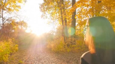 Güzel kız sonbahar Ormanda yürür. Parlak güneş ışığı. Ormanda günbatımı. Yakın çekim. Ağır çekim