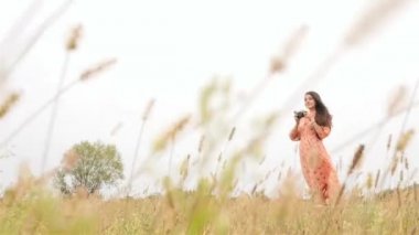 Güzel esmer ile bir fotoğraf makinesi. Elbise rüzgarda geliştirir. Ağır çekim. Yeşil çim. HD