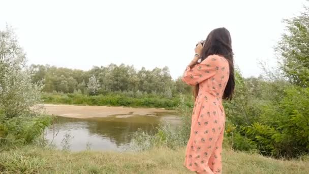 Una chica morena con el pelo largo fotografía el río. En cámara lenta. Hermoso paisaje — Vídeos de Stock