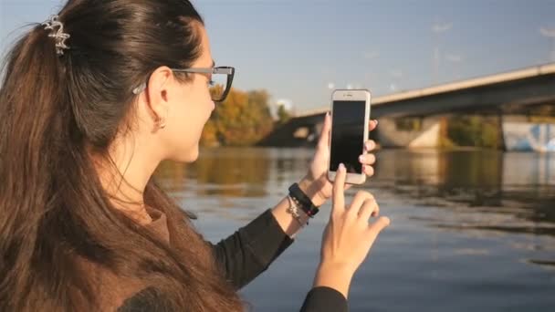 Kız telefonda fotoğraf yapıyor. Güzel doğa. Köprü olan nehir. Güneşli bir gün. Yavaş hareket — Stok video