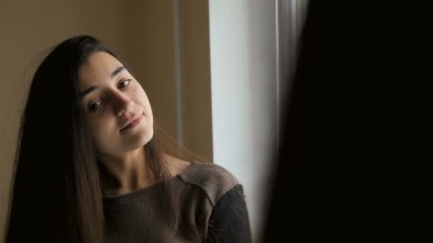 Girl combing hair near the mirror. Long dark hair. Close-up. Slow motion. Beautiful light from the window — Stock Video