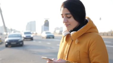 Elinde telefon olan bir kız. Arka planda arabalara binmek. Yavaş çekim