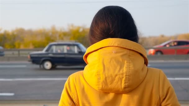 La fille se tient avec son dos à la caméra. Des voitures qui passent. Mouvement lent — Video