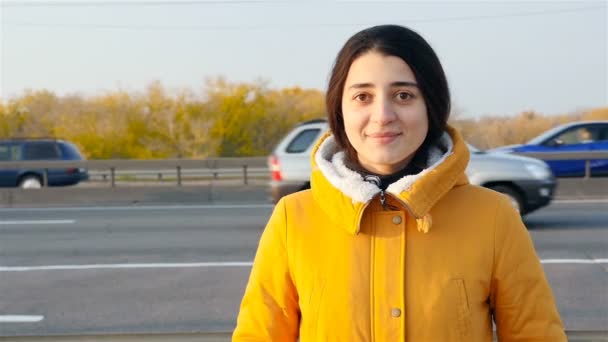 Beautiful brunette smiles at the camera. Close-up . Slow motion. Passing cars on the background — Stock video