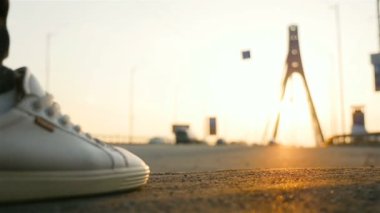 Şehir trafik arabalarının arka planında insan bacakları var. Yakın plan. Ağır çekim. Gün batımı. Asfaltta güneş ışığı