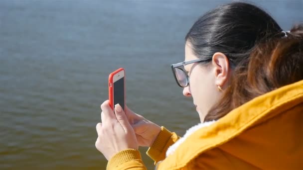 少女は川をスマートフォンで撮影する。接近中だ晴れた日。秋の天気 — ストック動画