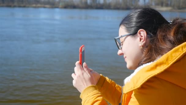 Hermosa chica fotografía el paisaje en un teléfono inteligente rojo. Primer plano. Movimiento lento . — Vídeos de Stock