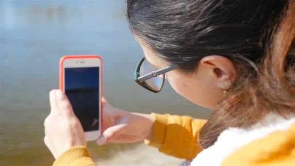 Krásná dívka fotografuje řeku s chytrým telefonem. Detailní záběr. Slunečné počasí na podzim — Stock video