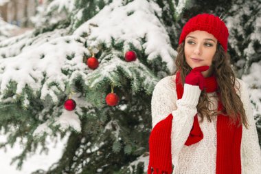 Noel ve yeni yıl kavramı. Kış vibes. Neşeli Noel ağacı yakınındaki eldiven ve kırmızı şapkalı kız. Uzay kopyalayın. portre