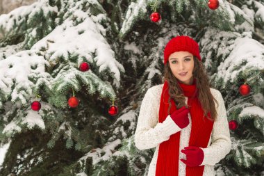 Noel ve yeni yıl kavramı. Kış vibes. Neşeli Noel ağacı yakınındaki eldiven ve kırmızı şapkalı kız. Uzay kopyalayın. portre