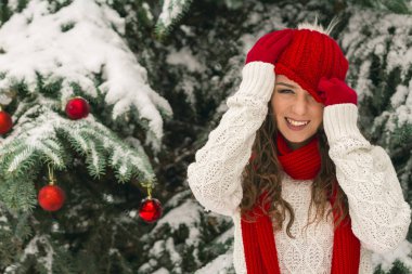 Noel ve yeni yıl kavramı. Kış vibes. Neşeli Noel ağacı yakınındaki eldiven ve kırmızı şapkalı kız. Uzay kopyalayın. portre