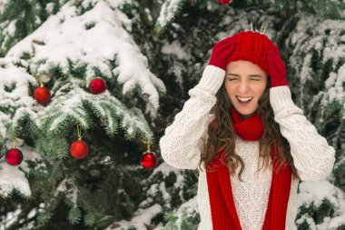 Noel ve yeni yıl kavramı. Kış vibes. Neşeli Noel ağacı yakınındaki eldiven ve kırmızı şapkalı kız. Uzay kopyalayın. portre