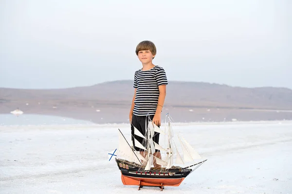 Boy standing near ship model on salt lake