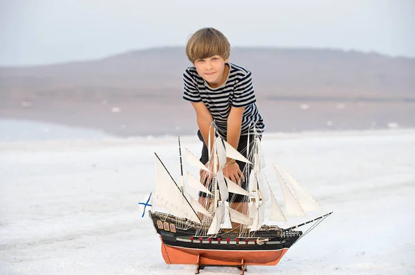 Boy standing near ship model on salt lake