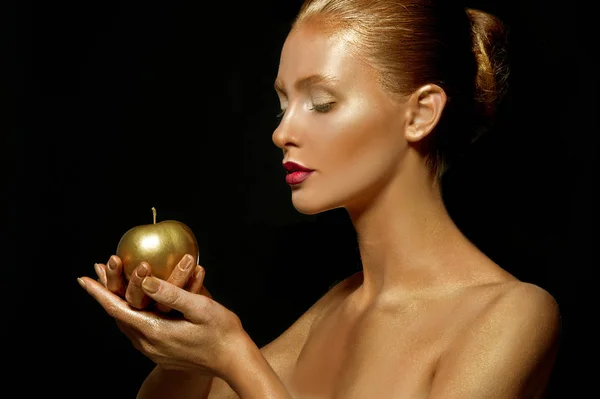 woman with golden make up and apple on black background