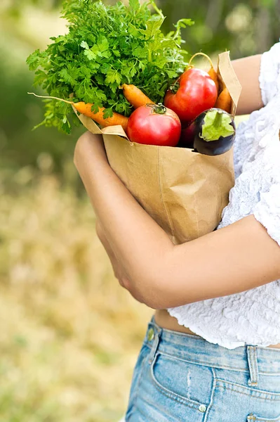 woman holding paper bag with fresh organic vegetables