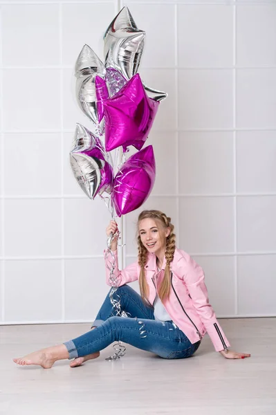 Beautiful woman with braided hair in a pink leather jacket sitting with balloons.