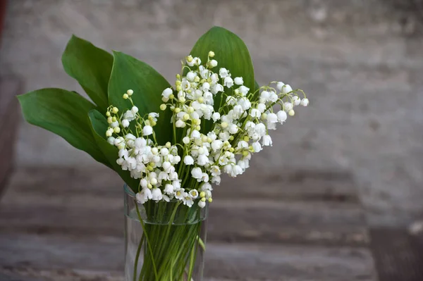 Spring bouquet of Lily of the valley in vase on wooden background. Decorative composition