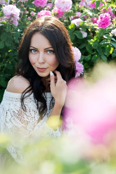 young woman in posing in pink roses field at daytime