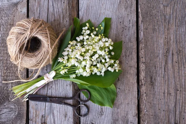Spring bouquet of Lily of the valley with twine and retro scissors on wooden background. Decorative composition