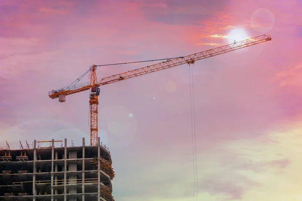 A lifting crane working on a construction site, a red sky background.