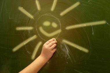 Çocuğun el tebeşir ile okul yönetimi üzerinde güneşin boyalar.