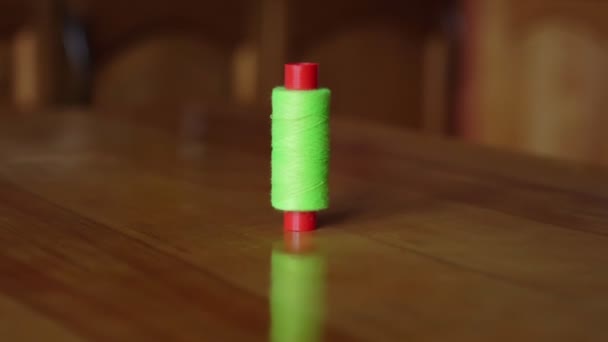 Зеленая нить на красной катушке стоит на коричневом деревянном столе — стоковое видео