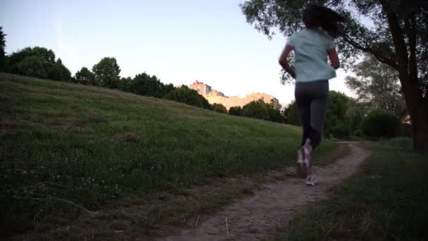 티셔츠와 레깅스를 입은 소녀가 녹색 공원 길을 따라 달리고 있습니다. — 비디오