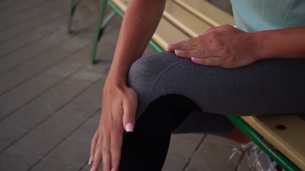 Sportieve dame in zwart grijs legging wrijft gekneusd knie met de hand — Stockvideo