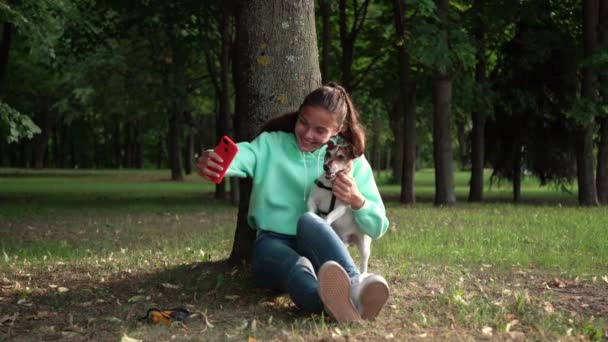 Bonita dama en sudadera con capucha y jeans hace selfie con perro — Vídeo de stock